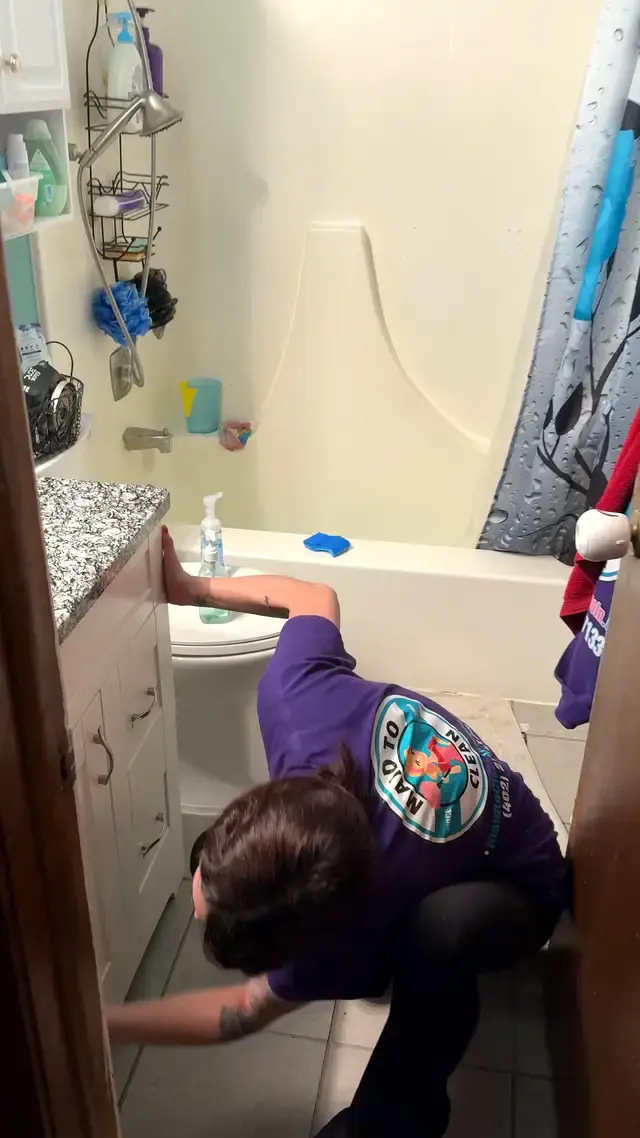 A Maid to Clean cleaner kneeling to scrub a bathtub and tile surround