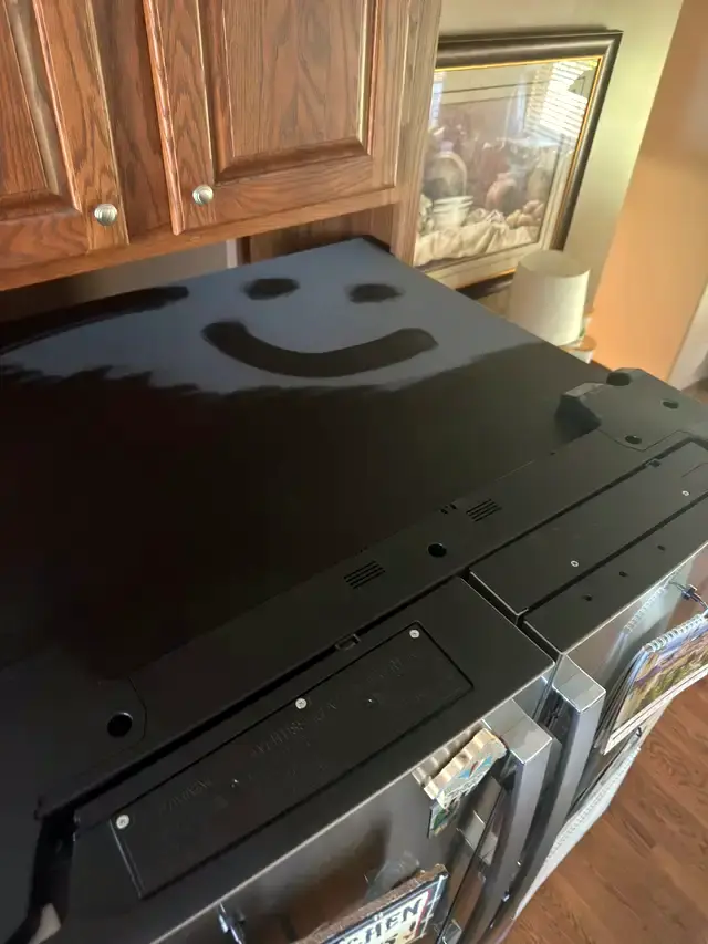 A smiley face drawn in the dust on top of a refrigerator